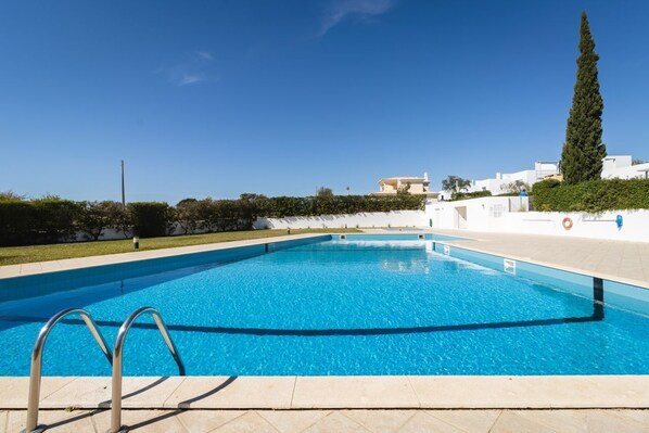 Une piscine à l’eau d’un bleu cristallin, entourée d’un mur blanc et d’une haie.