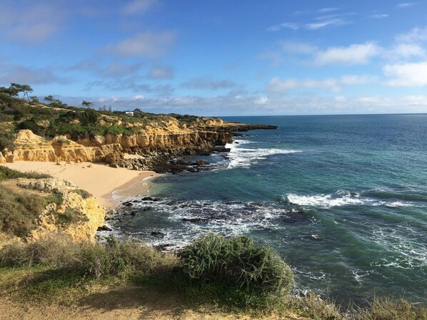 A coastal landscape with a sandy beach, rocky cliffs, and the ocean.