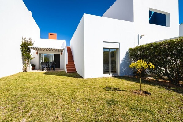 Une maison moderne avec une façade blanche, un patio couvert et un petit jardin.