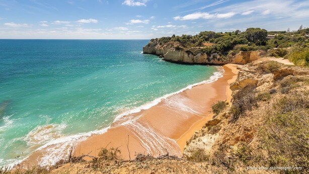 Un paisaje costero con una playa arenosa, acantilados rocosos y un cielo azul despejado.