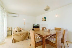 Une pièce comprenant une table à manger en bois, des chaises en osier, un canapé, un téléviseur et un ventilateur de plafond.