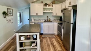 A modern kitchen with white cabinets, a stainless steel refrigerator, and a marble countertop. - The Garden Loft at Heavensfield (Rexburg)