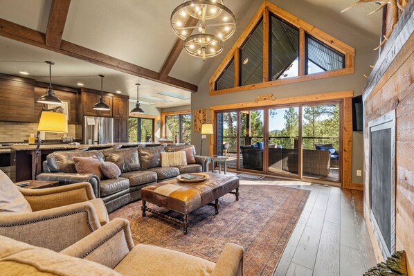 A spacious living area with a large sofa, a coffee table, and a fireplace. There are multiple windows providing natural light and views of the outdoors.