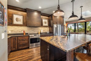 A modern kitchen with wooden cabinetry, a large island, stainless steel appliances, and pendant lighting.