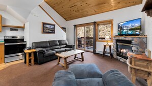 Ein gemütliches Wohnzimmer mit Kamin, einer schwarzen Ledersofa, einem Holztisch und einem Fernseher auf einem Steinkaminbrett.
