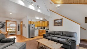Ein geräumiger Wohnbereich mit grauem Sofa, einem Holztisch und einer Küche im Hintergrund.