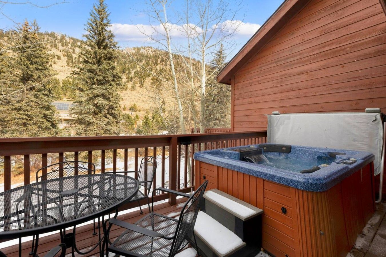 Una terraza de madera con un jacuzzi, una mesa de metal y sillas.