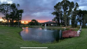 A serene lakeside setting with a gazebo, a small bridge, and a sunset in the background. - Heavensfield - Family Reunion Center (Rexburg)