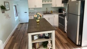 A modern kitchen with white cabinets, a stainless steel refrigerator, and a wooden island with a vase of flowers. - Heavensfield - Family Reunion Center (Rexburg)