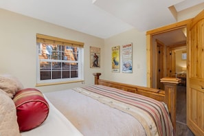 A bedroom with a bed, a window, wooden walls, and a door leading to another room. - Fall River Oasis • Private Hot Tub • RMNP (Estes Park)
