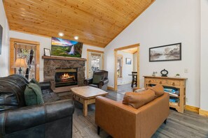 A cozy living room with a fireplace, leather sofas, a coffee table, and a television mounted above the fireplace. - Fall River Oasis • Private Hot Tub • RMNP (Estes Park)