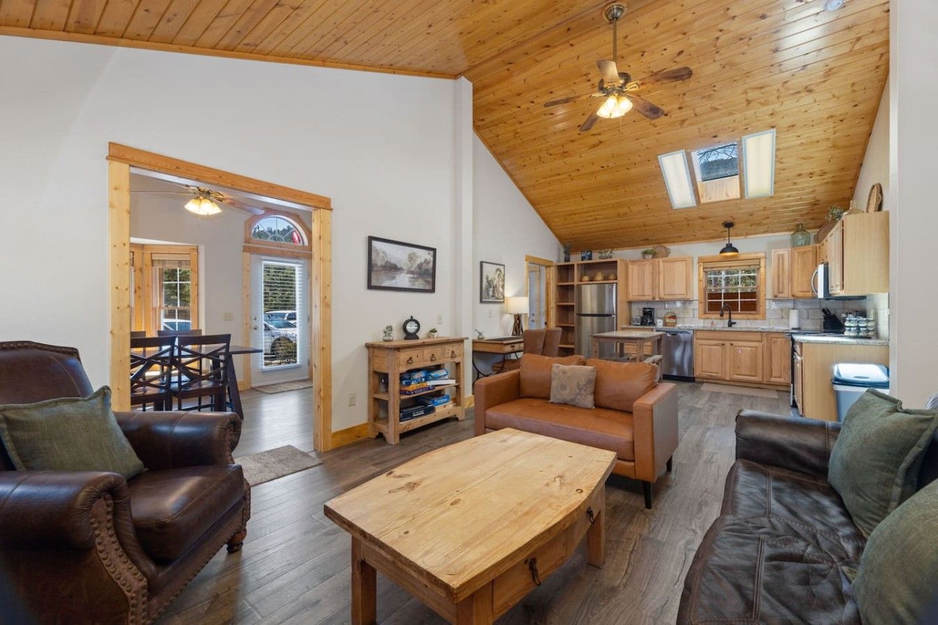 A spacious living area with a wooden ceiling, a dining table, leather sofas, and a kitchen with wooden cabinets.