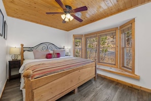 A bedroom with a wooden bed, a ceiling fan, and large windows. - Fall River Oasis • Private Hot Tub • RMNP (Estes Park)