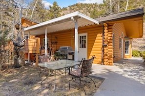 Une cabane en rondins dotée d’un patio couvert, d’un barbecue et d’une table à manger avec des chaises.