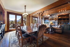 A spacious dining area with a large wooden table and chairs, a fireplace, and a view of the outdoors.