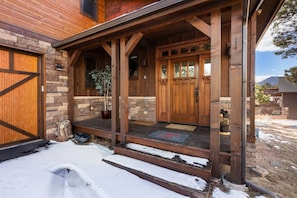 A wooden house with a stone facade, a front porch, and a snow-covered driveway.