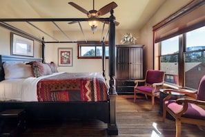Un dormitorio con cama con dosel, ventilador de techo, ventana grande con vistas y suelo de madera.
