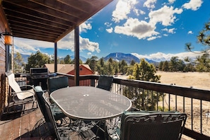 Un espacio exterior techado con una mesa, sillas, una parrilla y vistas a montañas.