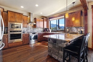 A modern kitchen with wooden cabinets, a large island, and a stone backsplash. - Large home near Lake Estes! (Estes Park)