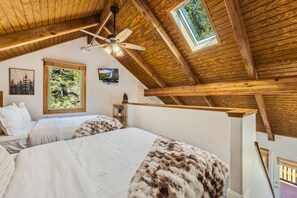 A bedroom with two beds, a ceiling fan, a TV, and a window with a view of trees. - Fall River Suite • River Views • Near RMNP (Estes Park)