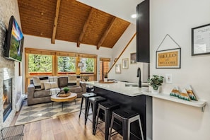 Una cocina moderna con techo de madera, una barra y una sala de estar con chimenea.