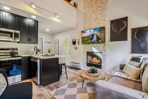 A modern kitchen with dark cabinets, a built-in oven, and a central island with a sink. - Fall River Suite • River Views • Near RMNP (Estes Park)