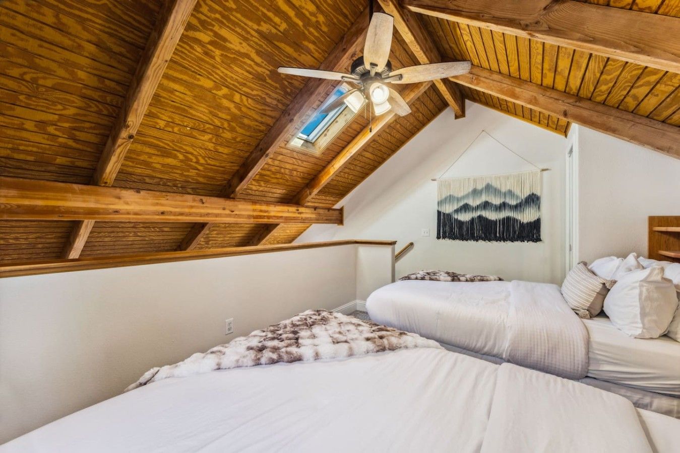 Un dormitorio con dos camas, vigas de madera, un ventilador de techo y un tapiz colgado en la pared.