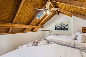 Un dormitorio con dos camas, vigas de madera, un ventilador de techo y un tapiz colgado en la pared.