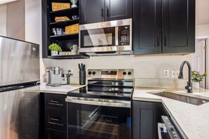 A modern kitchen with stainless steel appliances, black cabinetry, and a marble countertop. - Fall River Suite • River Views • Near RMNP (Estes Park)