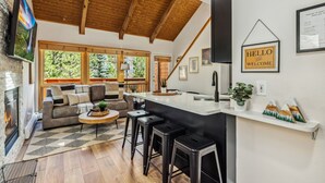 A modern kitchen with a wooden ceiling, a bar area, and a large window overlooking a forest. - Fall River Suite • River Views • Near RMNP (Estes Park)