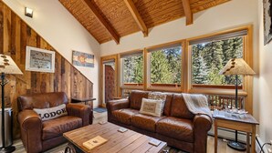 A cozy cabin interior with wooden walls and ceiling, two leather sofas, a wooden coffee table, and large windows offering a view of trees. - Fall River Suite • Serene • Close to RMNP (Estes Park)