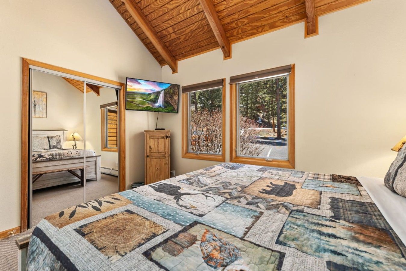 Un dormitorio con una cama grande, un televisor y vistas al exterior a través de tres ventanas.