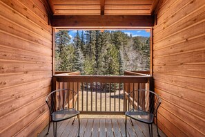 A wooden balcony with two chairs, overlooking a forested area.