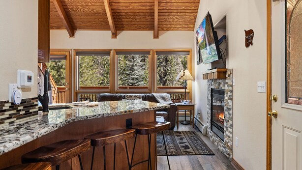 A kitchen with a bar area, wooden ceiling, large windows, and a fireplace. - Fall River Suite • Serene • Close to RMNP (Estes Park)