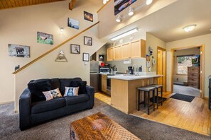 A modern interior with a sofa, a wooden coffee table, a kitchen with wooden cabinets, and a staircase.