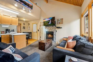 A cozy living room with a fireplace, a sofa, and a kitchen area with wooden cabinets.