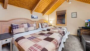 A bedroom with two beds, wooden ceiling beams, a nightstand, a desk, and a television.