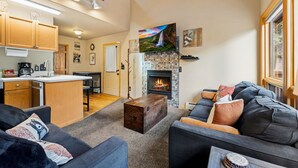 A modern living room with a fireplace, a sofa, a coffee table, and a kitchen area with wooden cabinets and a dining table.