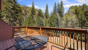 A wooden deck with a metal table and chairs, surrounded by a wooden fence and dense forest. - Peaceful Fall River Suite • Minutes to RMNP (Estes Park)