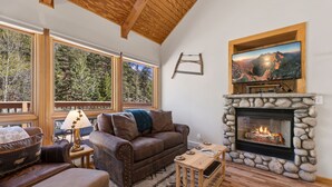 A cozy living room with a stone fireplace, a large TV mounted above it, and a comfortable brown leather sofa. - Peaceful Fall River Suite • Minutes to RMNP (Estes Park)