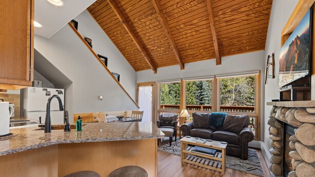 A modern kitchen with a wooden ceiling, a bar area with stools, a fireplace, and large windows offering a view of the outdoors. - Peaceful Fall River Suite • Minutes to RMNP (Estes Park)