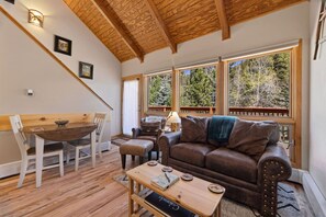 A cozy room with a wooden ceiling, a brown leather sofa, a wooden dining table with chairs, and large windows offering a view of trees. - Peaceful Fall River Suite • Minutes to RMNP (Estes Park)