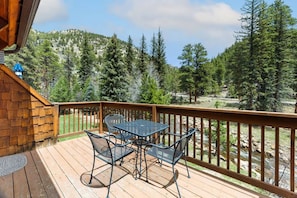 A wooden deck with a table and chairs, overlooking a mountainous landscape with trees.