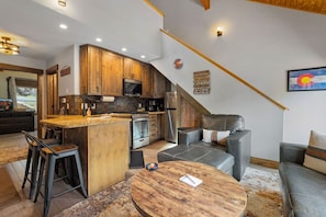 A modern kitchen with wooden cabinets, a built-in oven, and a dining area with a round table and bar stools. - Riverfront Haven • River Views • Near RMNP (Estes Park)