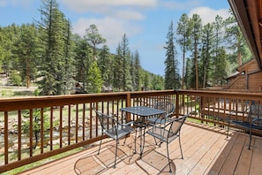 A wooden deck with a table and chairs, overlooking a forested area with a stream. - Riverfront Haven • River Views • Near RMNP (Estes Park)