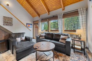A cozy living room with a fireplace, leather sofas, a coffee table, and large windows with curtains. - Riverfront Haven • River Views • Near RMNP (Estes Park)
