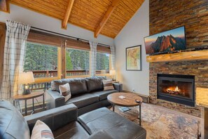 A cozy living room with a fireplace, leather sofa, and a large window overlooking a forest.