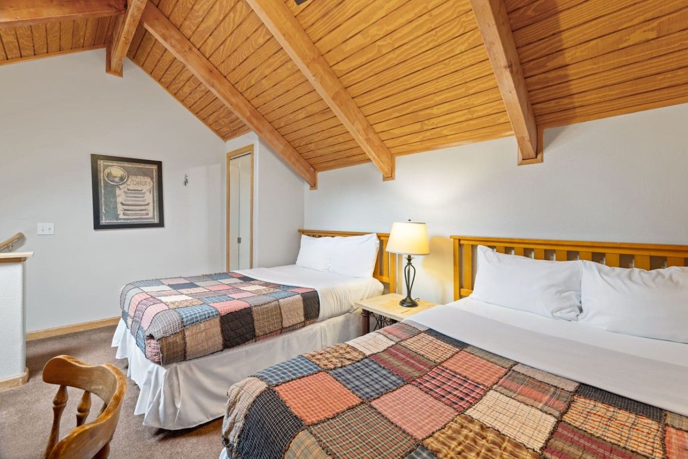 Una habitación con dos camas, techo de madera, un certificado en la pared y una silla.