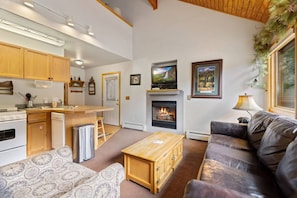 A living room with a fireplace, a sofa, a coffee table, and a television. - Cozy Riverfront Suite • Near RMNP • River Views (Estes Park)