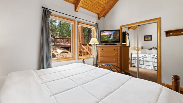 Ein Schlafzimmer mit einem großen Bett, Holzboden, einem Fernseher, einer Kommode und einem Spiegel, der den Raum widerspiegelt.